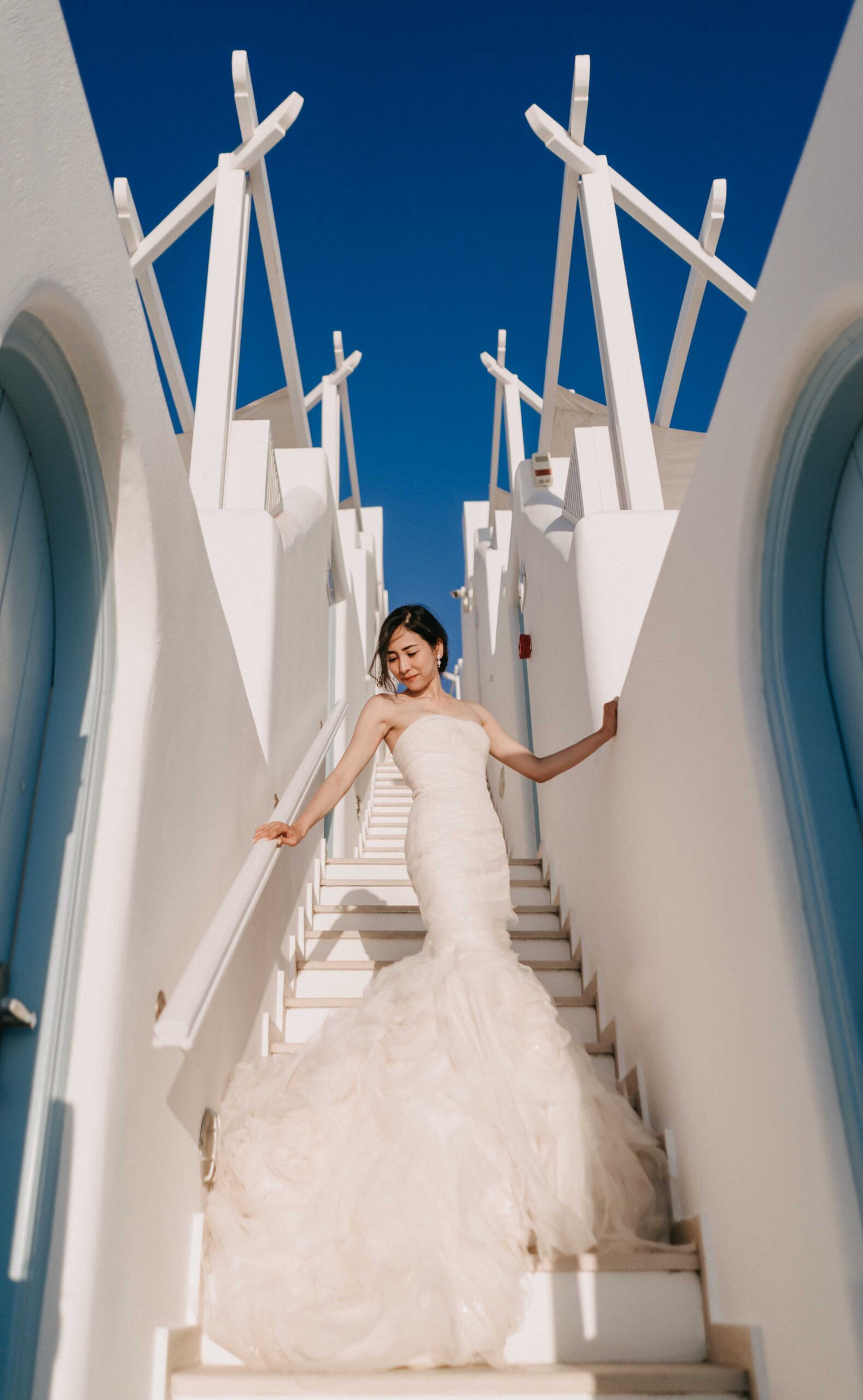 Bride descending an empty staircase in a quiet Santorini village.