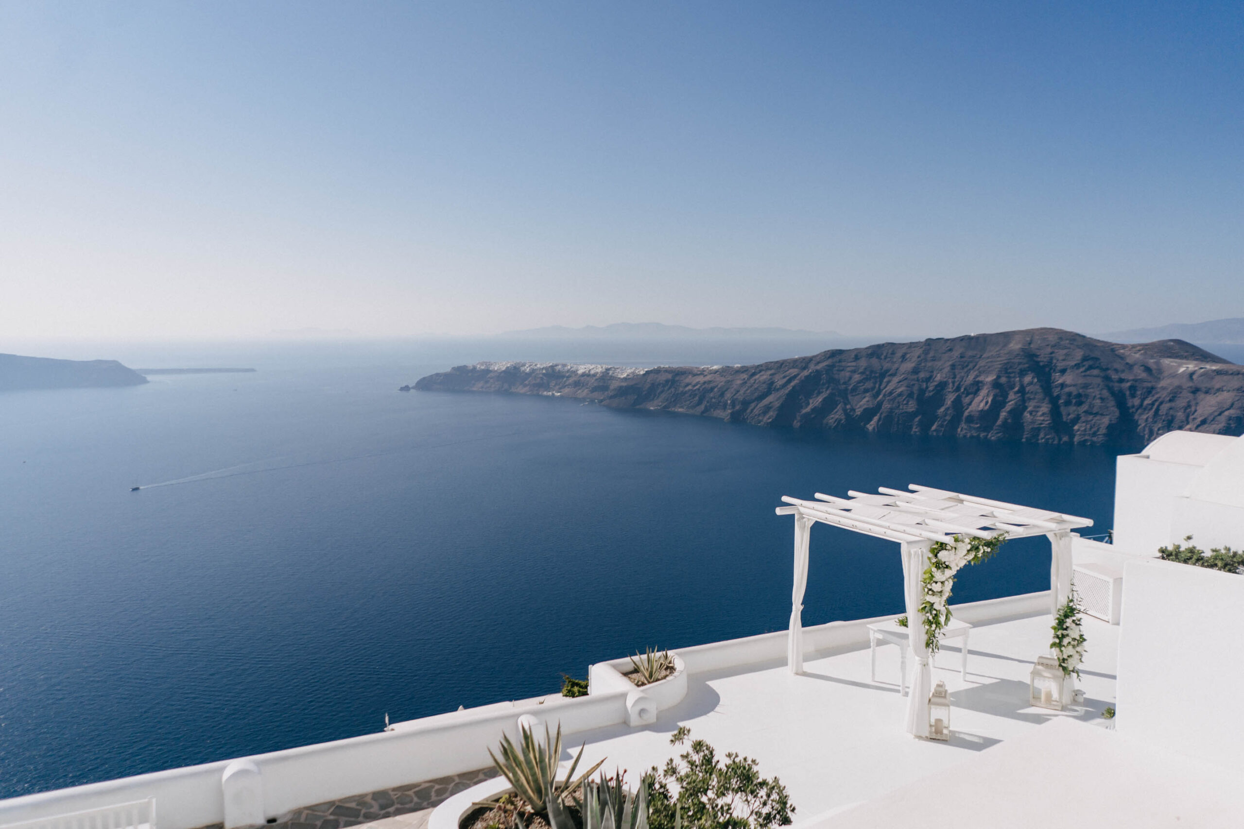 Wedding ceremony arch on a Santorini caldera terrace in afternoon light.