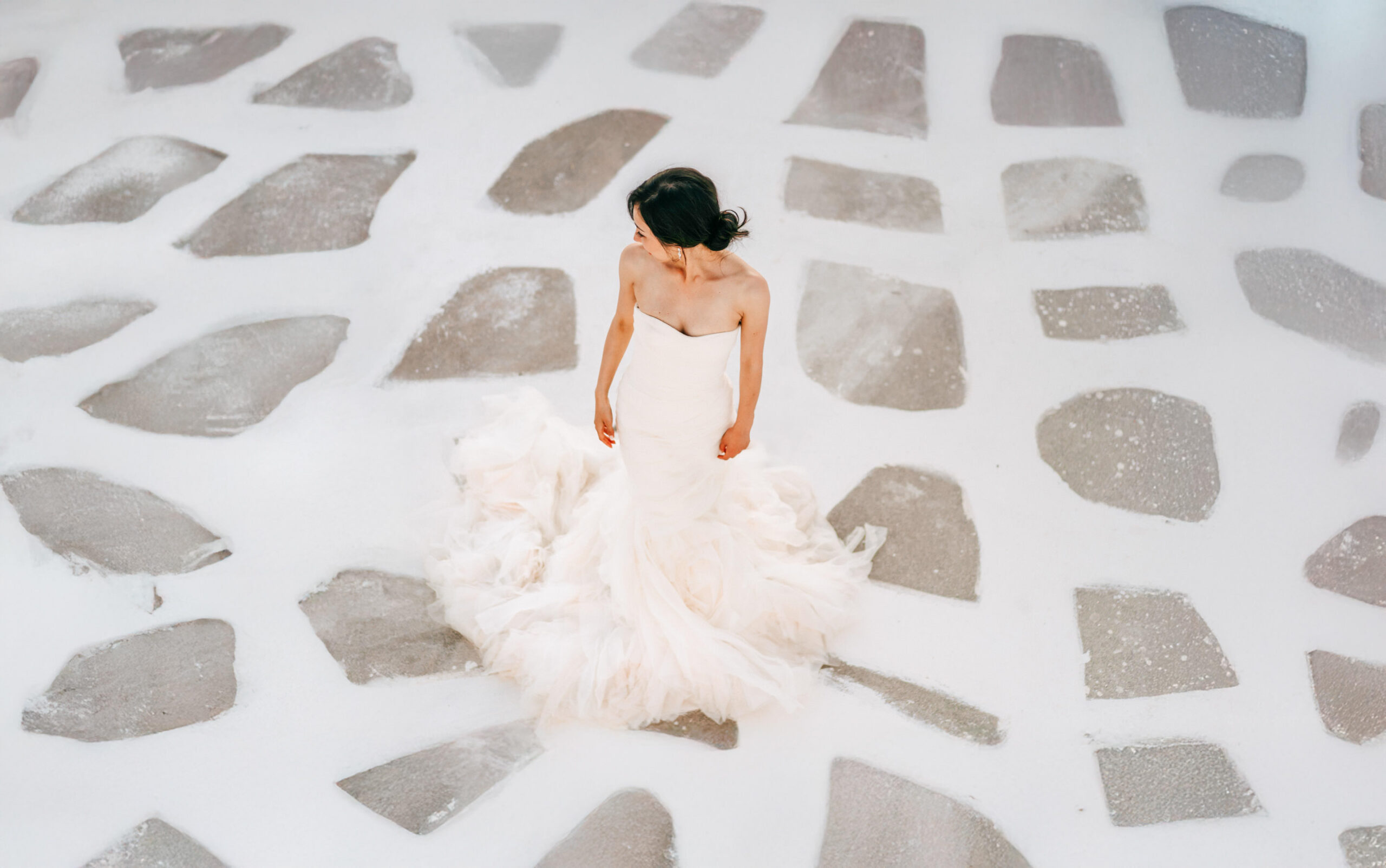 Bride on an empty patterned stone plaza in a Santorini village.