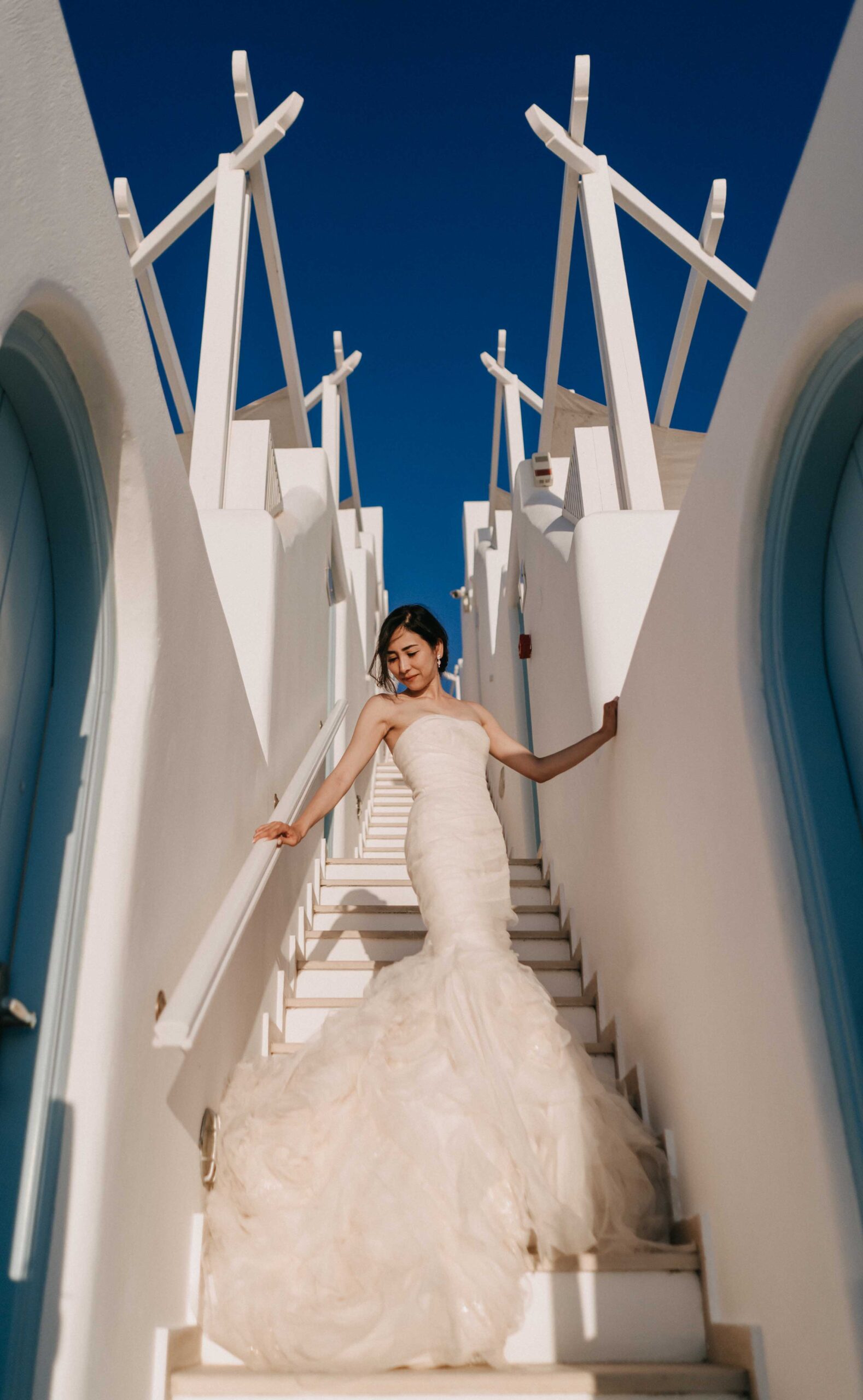 Bride on a white Santorini staircase in strong mid-morning light.