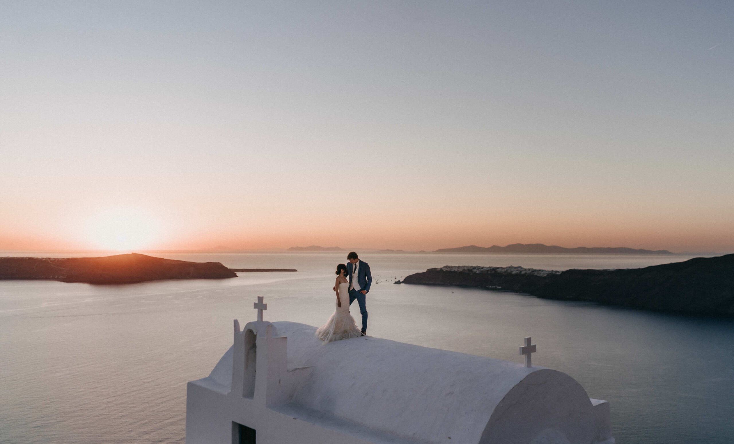 Couple at a quiet Santorini chapel at sunset in shoulder season.